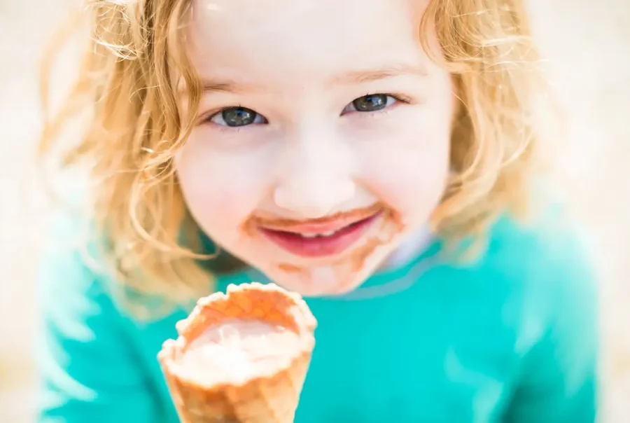 little girl holding ice cream cone up towards camera